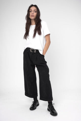 A woman wearing black striped cuffed slacks and a white shirt with a belt.
