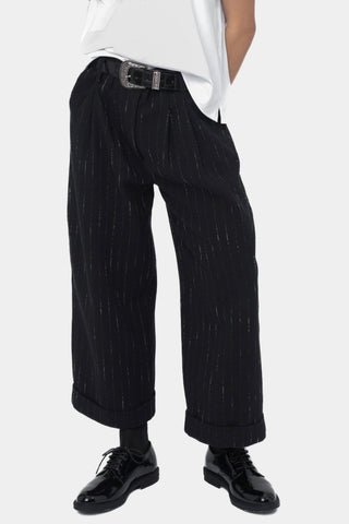 A person wearing black striped cuffed slacks and a white shirt with a belt.