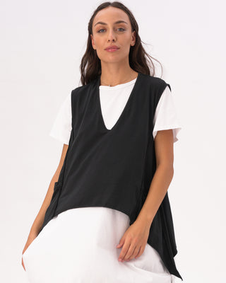 A woman wearing a black V-neck asymmetrical cotton pocket shirt with white pants.