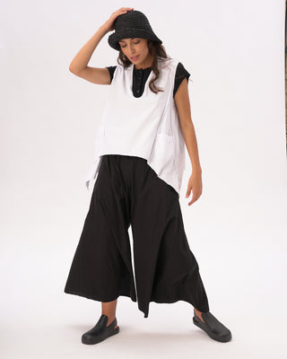 A woman wearing a white V-neck asymmetrical cotton pocket shirt with black pants and a black hat.