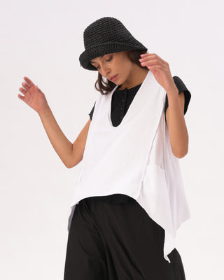 A woman wearing a white V-neck asymmetrical cotton pocket shirt with black pants and a black hat.
