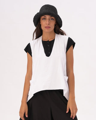 A woman wearing a white V-neck asymmetrical cotton pocket shirt with black pants and a black hat.